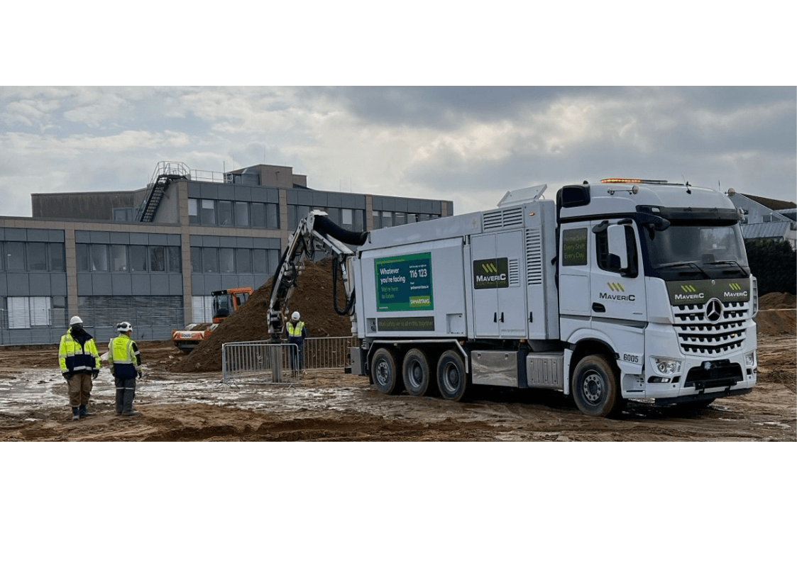 A Maveric excavator digging a shored, dewatered foundation within sheet-piled support on a live construction site.