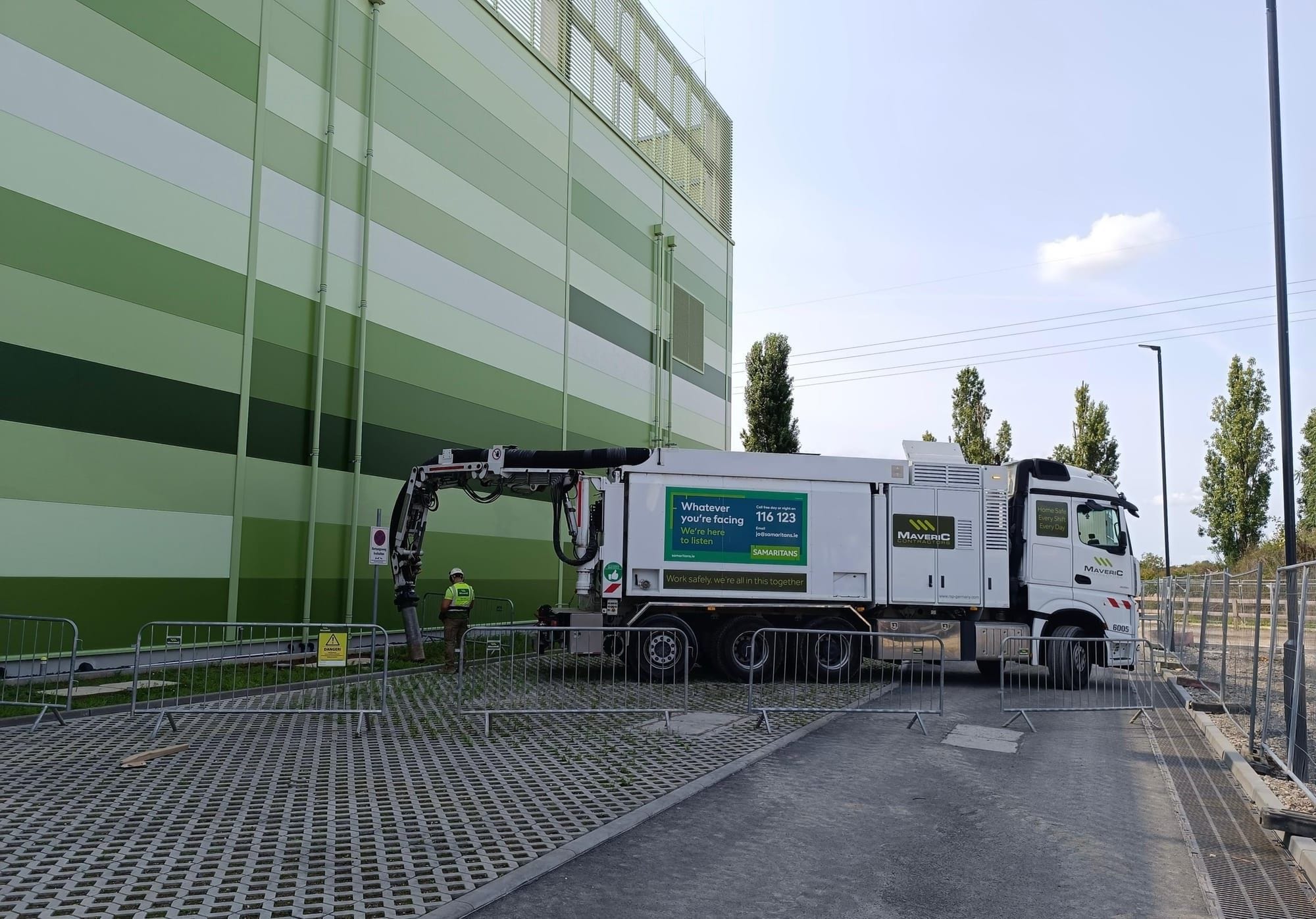 A Maveric vacuum-excavation truck with its suction boom deployed beside a data-centre building under construction.